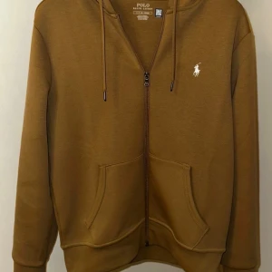 En hoodie från Ralph Lauren - Säljer en brun hoodie från Ralph Lauren, inköpt för tre veckor sedan i butiken. Den är i nyskick, endast använd ett fåtal gånger och självklart fri från fläckar eller skador. Du får med den kvitton och påsen.  Storlek: S Nypris: 2200 Mitt pris: 1299  Perfekt för dig som vill ha en stilren och bekväm hoodie av hög kvalitet! Skicka ett meddelande vid intresse. Kan mötas upp eller skickas mot fraktkostnad.  Först till kvarn! MVH/Sultan