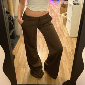 Bruna randiga kostymbyxor - Snygga bruna kostymbyxor med diskreta ränder. Byxorna har en lågmidjad passform och är utrustade med ett bälte baktill för extra stil. Passar en som är runt 170cm lång. Jag är 160cm