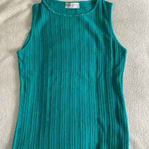 Turkos ribbad ärmlös topp - Snygg turkos ärmlös topp  med ribbad struktur och små pärldetaljer vid halsringningen. 