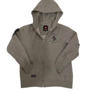 Grå Marine Sailing Club zip-up hoodie - Snygg grå zip-up hoodie från Marine Sailing Club. Den har en tryckt logga på bröstet och ärmen, samt en praktisk huva. Perfekt för en avslappnad stil. Igenkligen storlek XL men passar som S.
