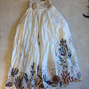 Vit långkjol med broderi - Säljer en vacker vit långkjol från Zara med färgglatt broderi i botten. Kjolen har ett elastiskt midjeband med zigzag-mönster i grönt och gult. Perfekt för en bohemisk look! Inte strukit den efter jag tvätta den så ni tänker på det, annars är den rakare. Säljer pågrund av flytt och för mycket kläder 🙃🙃🙃