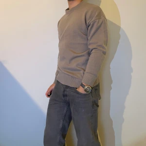 Beige stickad tröja - Säljer en stilren beige stickad tröja med rund hals och långa ärmar. Perfekt för en avslappnad look. Tröjan har ribbade muddar vid ärmslut och nederkant.