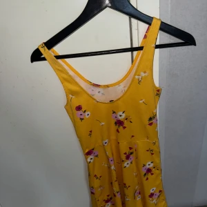 Gul blommig klänning - Säljer en söt gul klänning med blommigt mönster i rosa och vitt. Klänningen har smala axelband och en avslappnad passform, perfekt för soliga dagar. 🌼