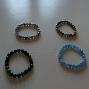 Fyra pärlarmband i olika färger - Säljer fyra stilrena pärlarmband i olika färger. Ett armband är vitt med svarta ådringar, ett är mörkgrönt, ett är ljusblått och ett är brunt. Perfekta för att matcha med olika outfits. 45kr styck om man vill köpa någon enskild.