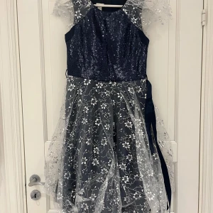Mörkblå glittrig klänning med spetsdetaljer - Säljer en fantastisk mörkblå klänning med glittriga paljetter och vackra spetsdetaljer. Klänningen har en elegant blommig spetsöverdel och ärmlös design. Perfekt för speciella tillfällen! 🌟