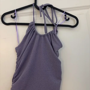 Lila topp från BikBok - Snygg lila topp från BikBok med smala axelband och en glittrig yta. Perfekt för att sticka ut med sin skimrande look. Toppen har en åtsittande passform och är tillverkad i ett mjukt material. Perfekt för fest eller finare event!☺️