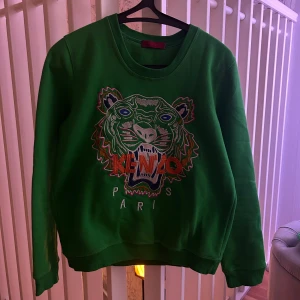 Kenzo Sweatshirt - Säljer en grön sweatshirt från Kenzo med ett broderat tigerhuvud och texten 'Kenzo Paris' på framsidan. Tröjan har långa ärmar och en rund halsringning. Perfekt för en cool och avslappnad stil. Köpt för många år sedan, bra skick, passar både herr och dam