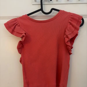 Röd ribbad topp från Zara - Säljer en söt röd ribbad topp från Zara med volangdetaljer på ärmarna. Toppen har en rund halsringning och är perfekt för en somrig look. Passar bra till både jeans och kjol. Corallfärgad.☺️