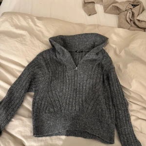 Grå stickad tröja från Gina Tricot - Säljer en mysig grå stickad tröja från Gina Tricot med dragkedja vid halsen. Perfekt för kyliga dagar med sin ribbade design och långa ärmar. Passar bra till både jeans och kjol.