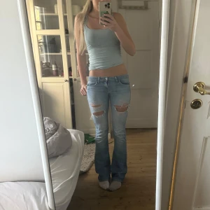 Ljusa bootcut lågmidjade jeans med slitningar - Snygga ljusa bootcut lågmidjade  jeans med slitningar på låren och knäna. De har en klassisk femficksdesign och är perfekta för en avslappnad stil. De är lite slitna och etiketten på ena fickan har åkt av. Synd på sista bilden.Midjemått:38 cm och innerbenslängden:85cm💕 Obs: de är lite slitna längst nere vid fötterna