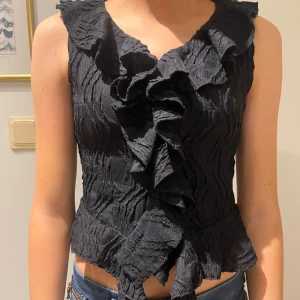 Svart volangblus - Snygg svart blus med volangdetaljer framtill. Storlek 152 men är som xxs. Helt oanvänd