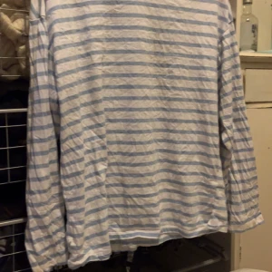 Randig långärmad tröja - Säljer en bekväm och stilren randig tröja i vitt och ljusblått. Tröjan har långa ärmar och en avslappnad passform, perfekt för en casual look. Passar bra till jeans eller shorts för en avslappnad stil.