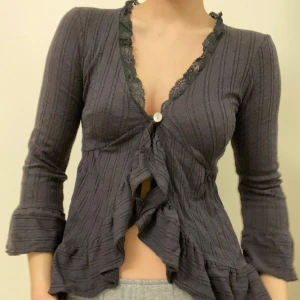 Söt grå topp med volanger - Super snygg kofta med spetsdetaljer vid halsen och volang framtill. Den är super bekväm och är i bra skick. Hör av dig om du har några frågor :)