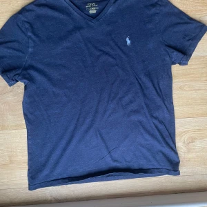 Mörkblå t-shirt från Ralph Lauren - Snygg mörkblå t-shirt från Ralph Lauren med v-ringning och broderad logga på bröstet. Perfekt för en stilren och avslappnad look.