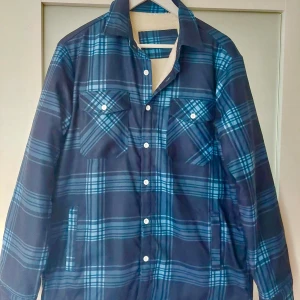 Flanellskjorta/ jacka overshirt fodrad herr - Flanellskjorta/jacka för kalla dagar. Helt ny aldrig använd, utan prislapp. Rutig mörkblå/ljusblå.  Storlek L Nypris 1495 kr