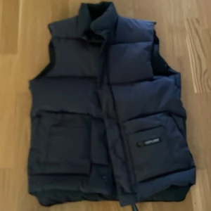 Vintage canada goose väst - Västen är storlek S och sitter som s/m  Den är i bra skick men har en liten skada på ryggen (kolla bild 3)  Såklart äkta och har mycket kvar att ge svart/mörk grå