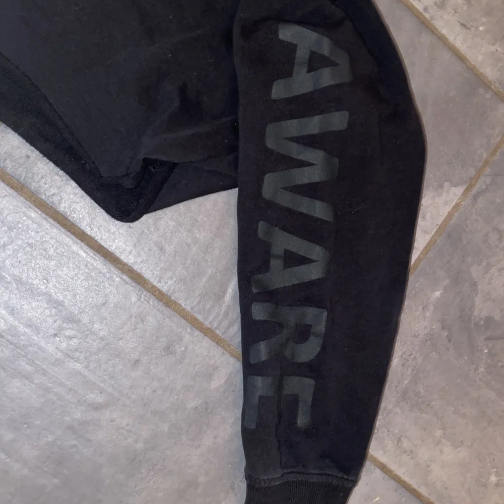 En croppad hoodie, jag klippte av den själv så kanten rullar upp sig. Står Aware på ena armen med stora bokstäver men är väldigt subtilt då texten är i svart. . Hoodies.