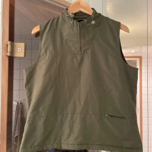 Grön väst från ZE-ZE Concept - Säljer en snygg olivgrön väst från ZE-ZE Concept i storlek L. Västen har en dragkedja framtill. Perfekt för höst och vår, och passar bra till både vardag och fritid.