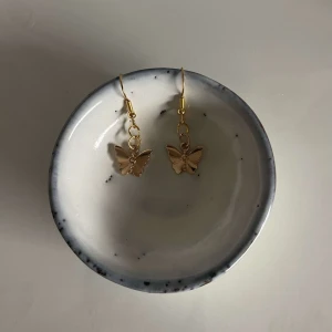 Guldiga fjärilsörhängen - Säljer ett par superfina guldiga örhängen med fjärilsdesign. De är hängande och har en liten kedja som ger dem en extra touch av elegans. Perfekta för att piffa upp vilken outfit som helst! 🦋✨