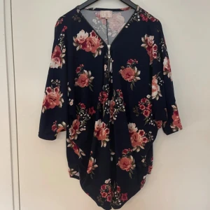 Blommig klänning med trekvartsärm - Säljer en superfin blommig topp med mörkblå bas och vackra rosor i rosa och rött. Toppen har trekvartsärmar och en bekväm passform, perfekt för både vardag och fest. Den är gjord i ett mjukt och skönt material som känns härligt mot huden.