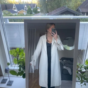 Lång creamvit kappa  - Lång creamvit kappa från Chiara Forthi i storlek 40. Den är använd ett fåtal gånger men i superfint skick! Den är superskön och varm! Kappans innertyg är i silkes liknande material, de är samma material i fickorna. Kappan har guld detaljer på armarna