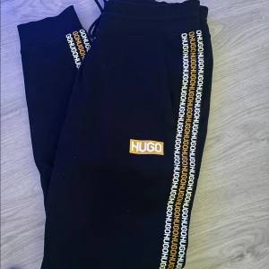 Hugo Sweatpants M - Snygga mjukisbyxor i svart färg med vit/gula detaljer. Storlek M Mycket fint skick!