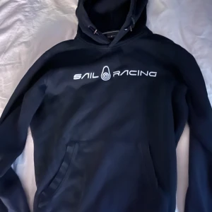 Sail Racing Hoodie - Sail racing hoodie med insydd text, använd ganska mycket men är i väldigt bra skick 8-9/10, ny pris 1300kr Tröjan är i storlek M men passar även bra på S