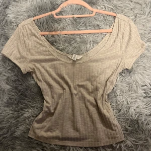 Beige ribbad topp från HM - Säljer en superfin beige ribbad topp från HM. Den har en v-ringad design och korta ärmar, perfekt för både vardag och fest. Toppen är i ett mjukt och stretchigt material som sitter snyggt på kroppen. Passar perfekt till jeans eller kjol!