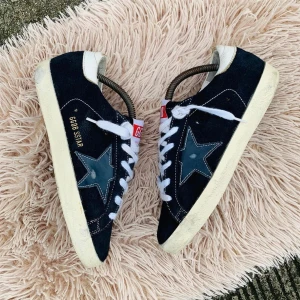 Svarta sneakers från Golden Goose - Snygga svarta sneakers från Golden Goose med vit sula och stjärndetalj på sidan. Skorna har vita snören och en röd etikett på plösen. Perfekta för en avslappnad stil.