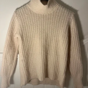 Beige stickad polotröja - Mysig beige stickad polotröja med ribbad krage och långa ärmar. Perfekt för kyliga dagar och ger en stilren look. Passar bra till både jeans och kjol.