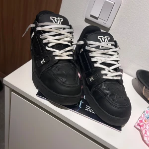 Svarta sneakers från Louis Vuitton - Snygga svarta sneakers från Louis Vuitton med vita snören och märkets logotyp på tungan. Skorna har en stilren design med diskreta detaljer och är perfekta för en trendig look. Skorna rengörs extra någrant innan dem skickas iväg