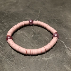 Rosa armband med lila pärlor - Charmigt armband med små rosa skivor och tre lila pärlor som ger en fin kontrast. Perfekt för att lägga till en färgklick till din outfit.