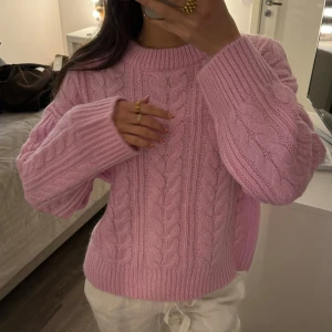 Rosa stickad tröja - Säljer en mysig rosa stickad tröja med kabelstickat mönster. Tröjan har långa ärmar och en rund halsringning. Perfekt för kyligare dagar och ger en stilren look. Passar bra till både jeans och kjol. Den är i storlek XS men är väldigt oversize i storleken.