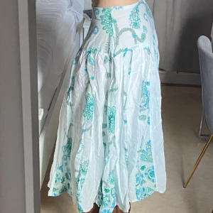 Vit och turkos långkjol - Charmig långkjol i vitt med turkosa och gröna mönster. Kjolen har en luftig och bekväm passform, perfekt för varma dagar. Den har ett vackert paisleymönster som ger en bohemisk känsla. Jag är 168cm lång. 