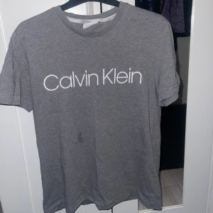 Calvin Klein T shirt - Säljer en stilren grå t-shirt från Calvin Klein . T-shirten har en klassisk passform och är tillverkad i mjukt bomullsmaterial. Väldigt lätt och mer eller mindre en helt vanlig Calvin Klein T-shirt. Inte använt nu ett tag,så tänkte varför inte bara sälja den. Den är i storlek M och i bra skick. Vid frågor om den så är det bara att skriva:)