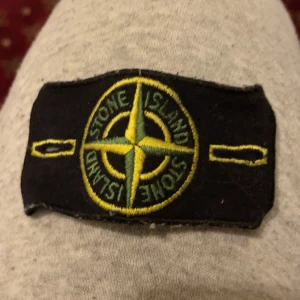 Grå och blå tröja från Stone Island - Säljer två tröjor från Stone Island. Den ena är en grå kortärmad t-shirt med det klassiska Stone Island-märket broderat på framsidan. Den andra är en blå långärmad tröja med rund hals och en knappdetalj på axeln. Båda tröjorna har den ikoniska Stone Island-loggan. Priset kan diskuteras ena är storlek s  och den ena m men båda sitter väldigt bra på