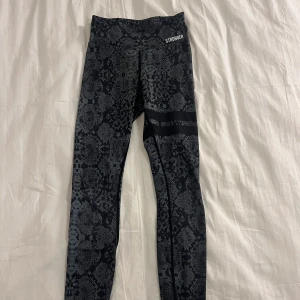 Stronger byxor - Snygga svarta leggings från Stronger med ett coolt ormliknande mönster. Perfekta för träning eller en avslappnad dag. De har en tight passform och är tillverkade i ett stretchigt material för bästa komfort.