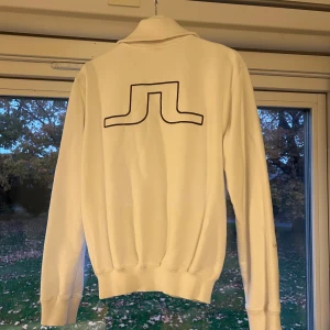 Vit tröja med dragkedja från J.Lindeberg - Säljer en stilren vit tröja från J.Lindeberg med dragkedja framtill. Tröjan är i M, men passar S.