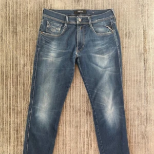 Blå jeans från Replay Anbass - Snygga blå jeans från Replay med en riktigt skön wash.  Har en klassisk femficksdesign och en diskreta slitningar för en trendig look. De har en slimmad passform och är modell anbass, vilket gör dem perfekta för en avslappnad stil. Liten anmärkning på ungefär en cm under gylfen/ grenen, annars mycket bra skick🙌💯