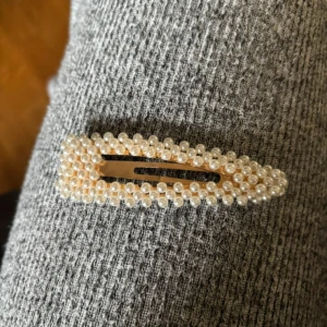 Hårklämma med pärlor - Elegant hårklämma dekorerad med små vita pärlor. Perfekt för att ge en stilfull touch till din frisyr. Klämman har en avlång form och är lätt att använda.