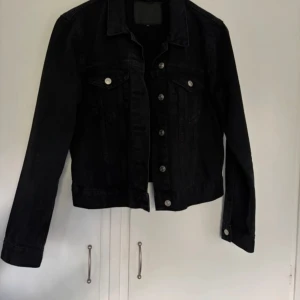 Svart jeansjacka - Snygg svart jeansjacka från lager 157 med klassisk design och silverfärgade knappar. Jackan har långa ärmar och två bröstfickor med knappstängning. Perfekt för en stilren look.