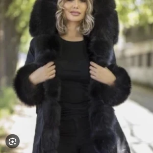 garrof jacka - Elegant svart fusk pälsjacka med stor huva och fluffiga detaljer runt ärmslut och framkant. Perfekt för att hålla sig varm och stilren under kyliga dagar. 