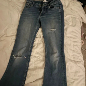 Blå jeans med slitningar - Säljer ett par blå jeans med coola slitningar. De har en klassisk femficksdesign och en knappgylf. Perfekta för en avslappnad stil. St 152 men passar även 158 perfekt.