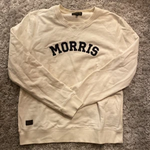 Vit Morris sweatshirt - Säljer en stilren vit sweatshirt från Morris med svart text på bröstet. Tröjan har långa ärmar och en klassisk rund halsringning.🖤den är i väldigt bra skick och passar till det mesta. Skriv gärna över frågor och funderingar, priset kan diskuteras.