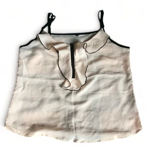 Beige linne med volangdetalj - Snyggt baby rosa linne med svarta axelband och volangdetalj framtill. Linnet har en dragkedja i mitten och svarta kanter som ger en fin kontrast.