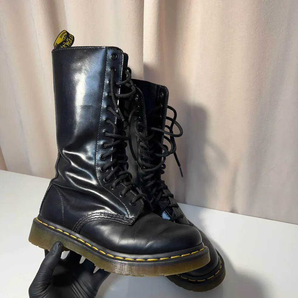 Snygga svarta boots i skinn med klassisk snörning och gul söm längs sulan. Perfekta för en tuff och stilren look. De har en praktisk dragflik baktill för enkel påtagning.. Kengät.