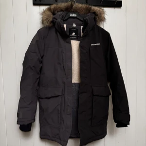 Svart parkajacka från Didriksons - Säljer en svart parkajacka från Didriksons med avtagbar fuskpäls på huvan. Jackan är 100% vattentät och har långa ärmar samt praktiska fickor framtill. Perfekt för kalla och blöta dagar.  Jackan är jämn i färgen men en skugga 