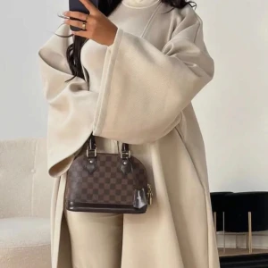 Beige kappa onesize - Säljer en stilren beige kappan med en elegant omlott-design. Den har vida ärmar och en lös passform som ger en chic look. Perfekt för höst och vår. Enkelt att matcha med olika outfits.