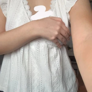 Vit spets topp - Charmig vit topp med spetsdetaljer och v-ringad design. Toppen har en omlottstil och korta ärmar, perfekt för sommarens festligheter. Den har en luftig passform och är tillverkad i ett lätt material.