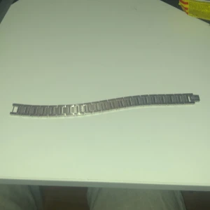 Silverfärgat armband från Lacoste - Stilrent silverfärgat armband från Lacoste med den ikoniska krokodilloggan. Armbandet har en länkdesign som ger en modern och elegant look. Perfekt för att komplettera din outfit med en touch av klass.